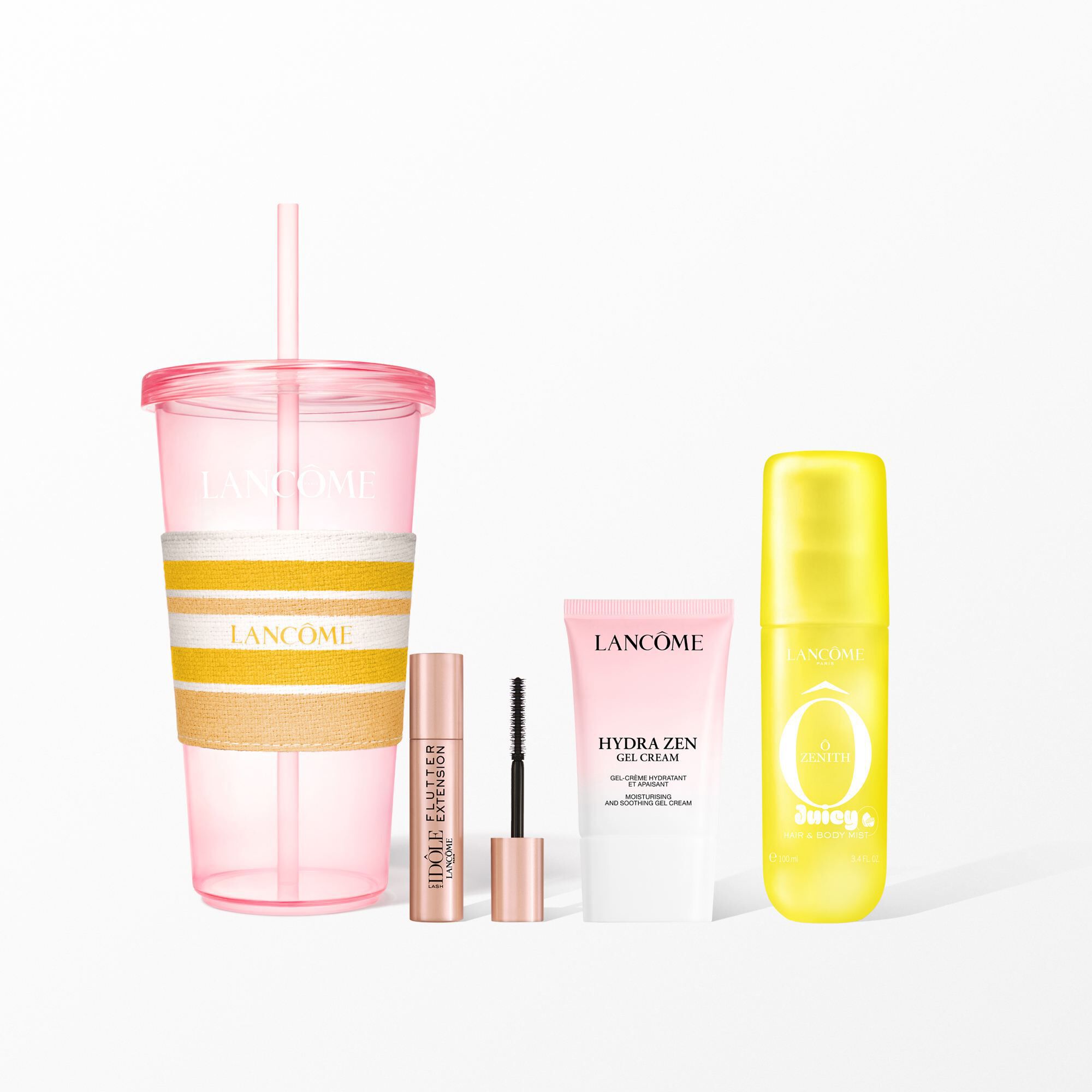 Un set de belleza Lancome con un vaso rosa reutilizable con una faja de rayas amarillas, mascara de pestanas, crema facial y una niebla amarilla para el pelo y el cuerpo.