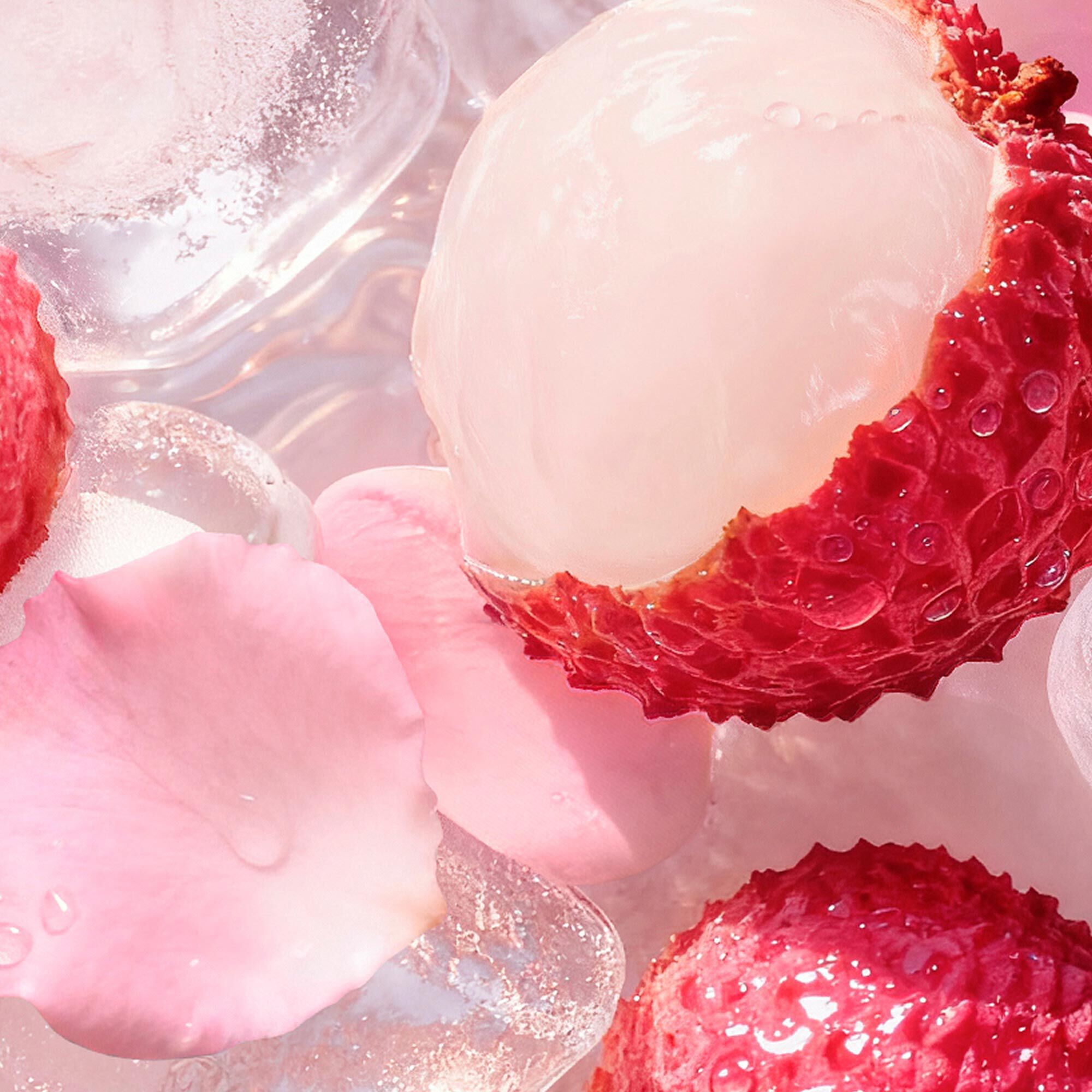 Litchis y petalos de rosa en una nevera rellena de cubitos de hielo. Al lado, una paleta rosa y una toalla rosa a rayas sobre fondo arenoso.