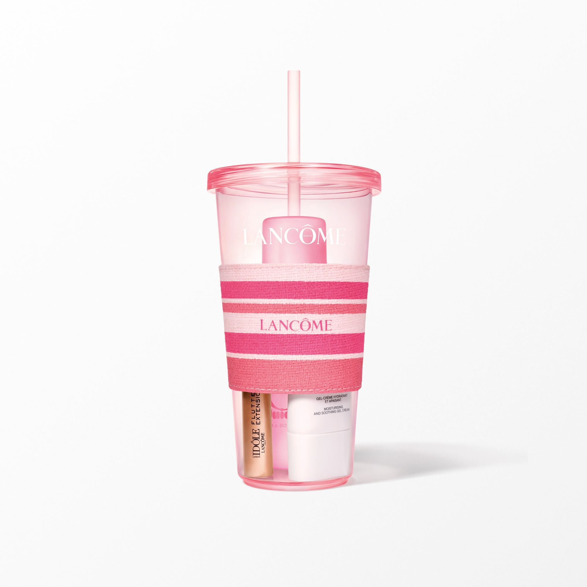 Un primer plano del vaso rosa Lancome con una faja de rayas rosas y blancas que contiene productos de belleza.
