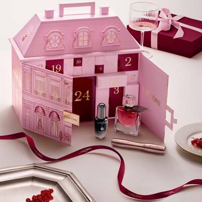 Un calendario de adviento abierto rosa de Lancome para casas adosadas con productos de belleza y una cinta roja.