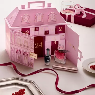 Un calendario de adviento abierto rosa de Lancome para casas adosadas con productos de belleza y una cinta roja.