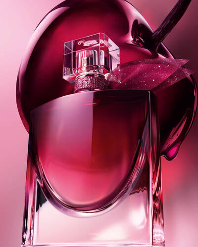 Un primer plano artistico del frasco de perfume burdeos situado delante de una gran cereza oscura y brillante.