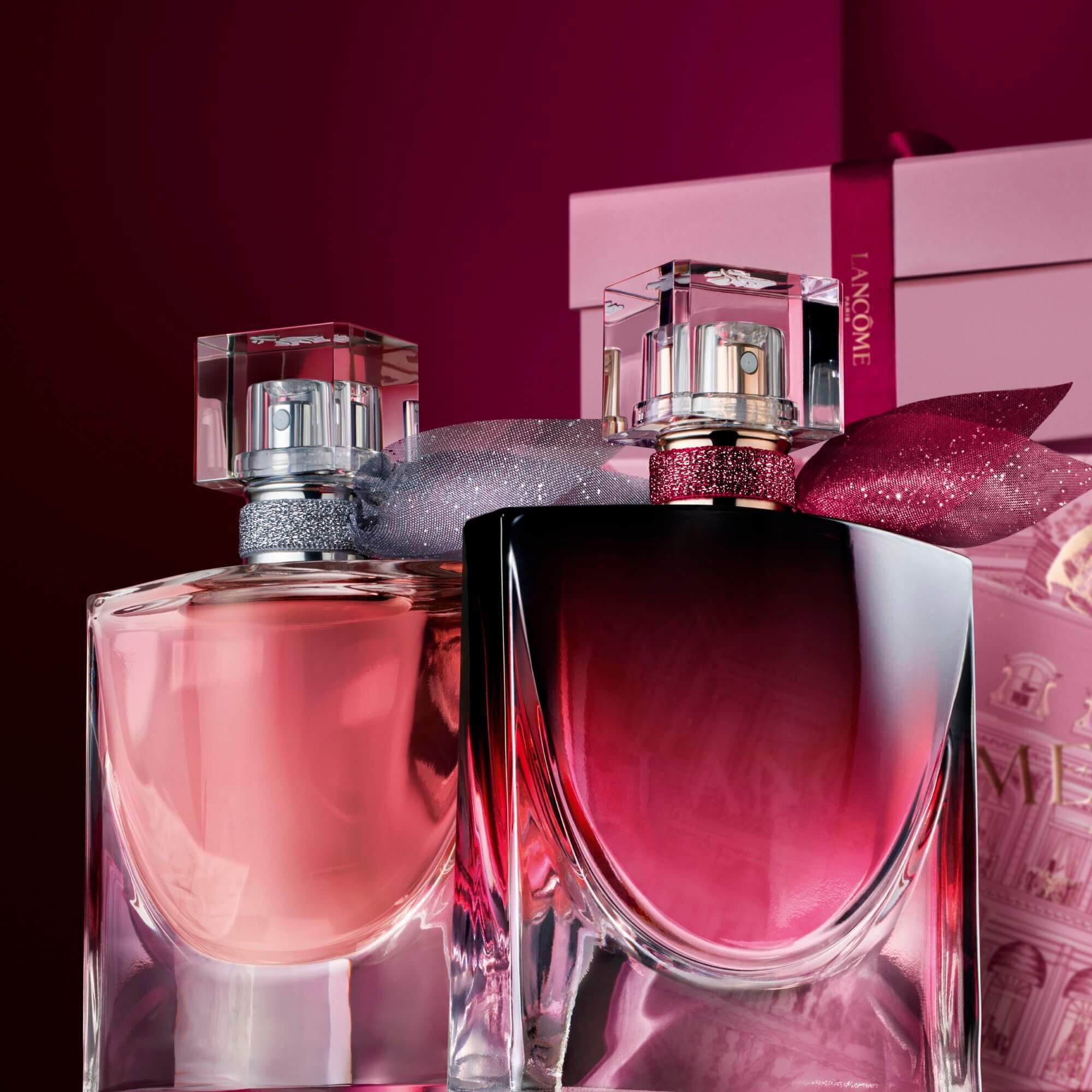 Imagen de La vie est belle EDP y La vie est belle L'Elixir Very Cherry de pie frente a un monton de cajas de regalo rosas y rojo oscuro, sobre un fondo rojo oscuro.