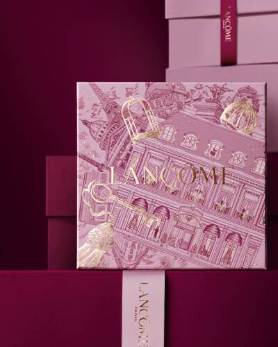 Imagen de una caja de regalo rosa Lancome de pie delante de un monton de cajas de regalo rosas y rojo oscuro, sobre un fondo rojo oscuro.