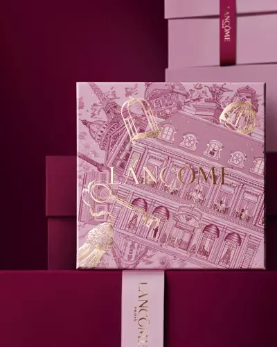 Imagen de una caja de regalo rosa Lancome de pie delante de un monton de cajas de regalo rosas y rojo oscuro, sobre un fondo rojo oscuro.