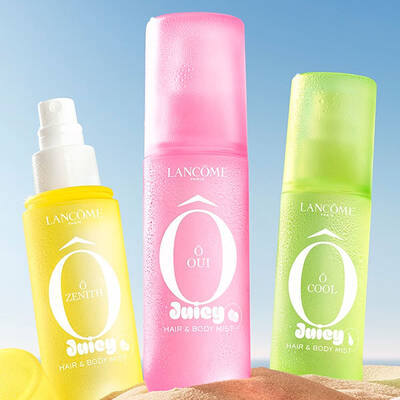Dos botellas amarillas, una botella rectangular de perfume con un diseno texturizado y otra botella de spray con un tapon amarillo en el lateral, situada en una playa de arena. Una toalla de playa doblada de rayas rosas esta junto a las botellas. Al fondo, hay un cielo azul despejado y el oceano.