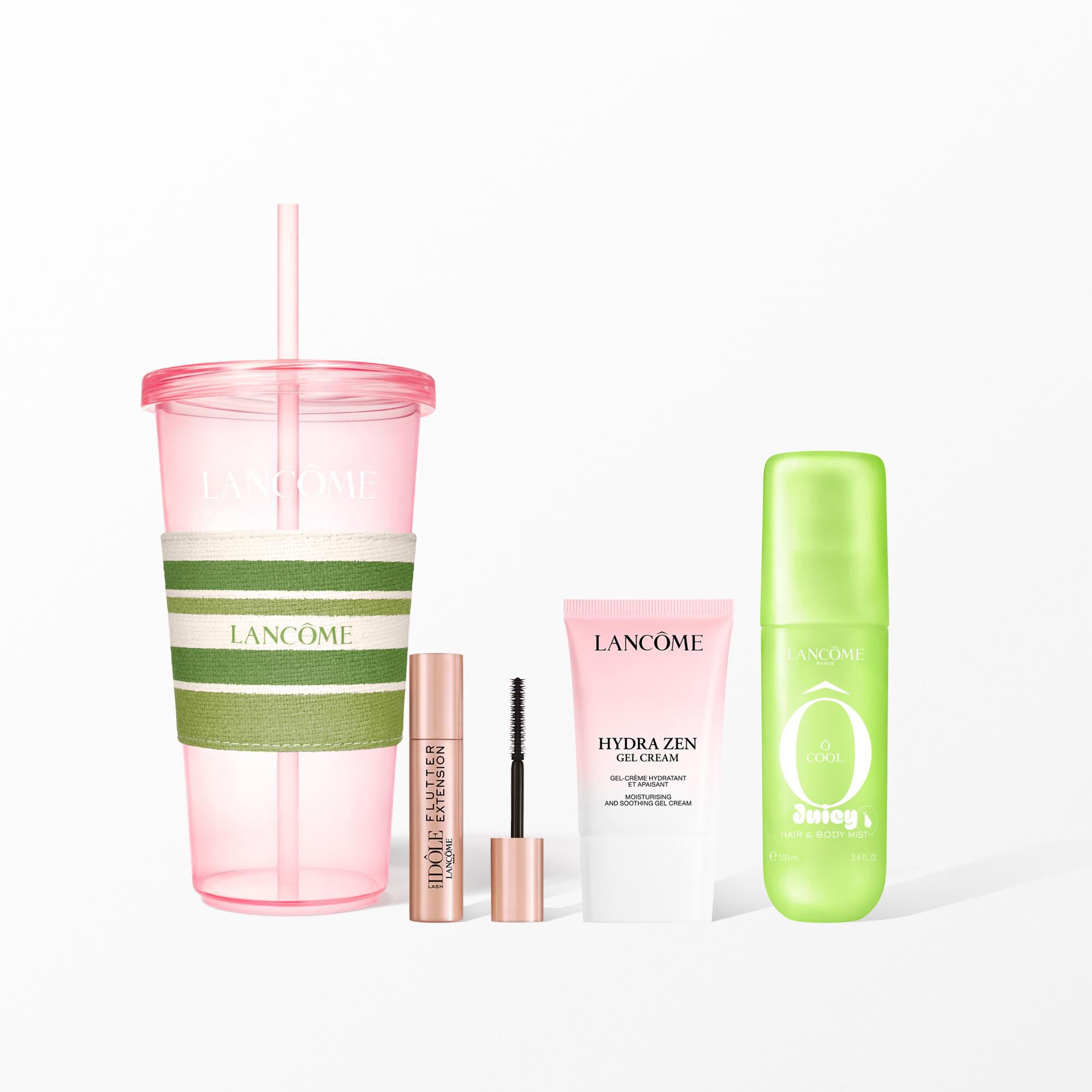 Un set de belleza de Lancome con un vaso reutilizable rosa con una faja de rayas, mascara de pestanas, crema facial y un bruma verde para el pelo y el cuerpo.