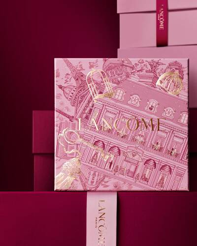 Imagen de una caja de regalo rosa Lancome de pie delante de un monton de cajas de regalo rosas y rojo oscuro, sobre un fondo rojo oscuro.