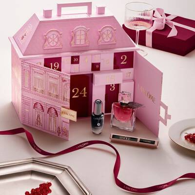 Un calendario de adviento abierto rosa de Lancome para casas adosadas con productos de belleza y una cinta roja.