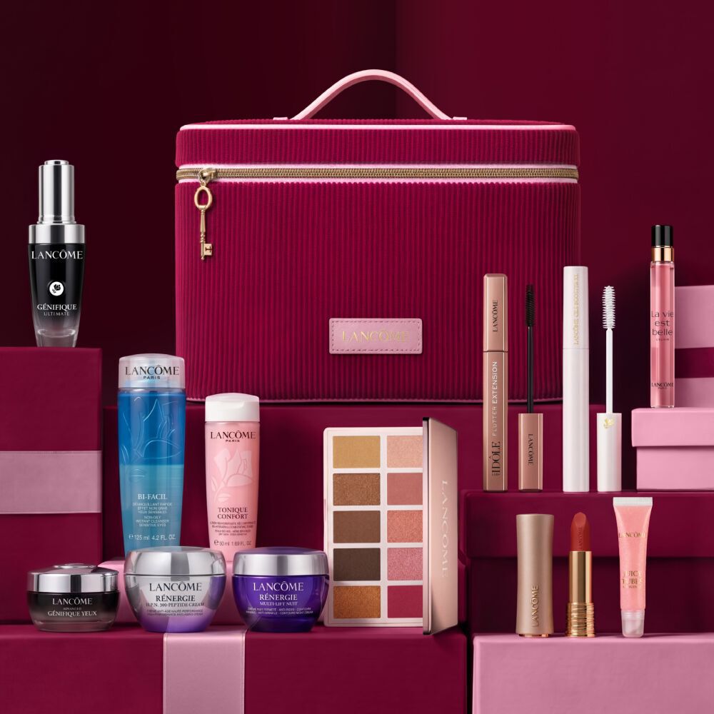Una naturaleza muerta festiva que muestra los productos Holiday Beauty Box de Lancome, dispuestos en cajas de regalo rosas y rojo oscuro alrededor de un tocador rojo cereza.