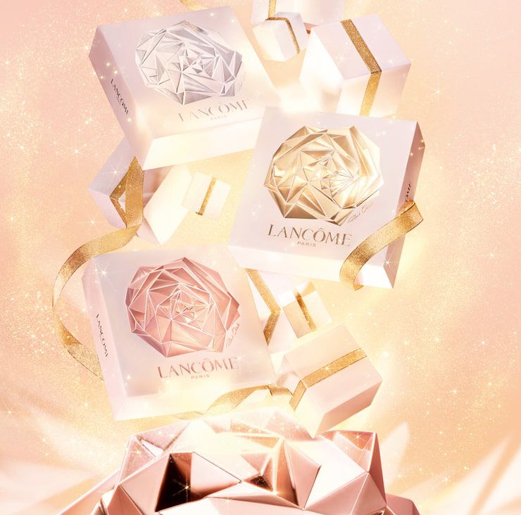 Tres cajas de regalo de Lancome con diseno geometrico en tonos blanco y dorado, adornadas con cintas brillantes sobre un fondo brillante y suave.