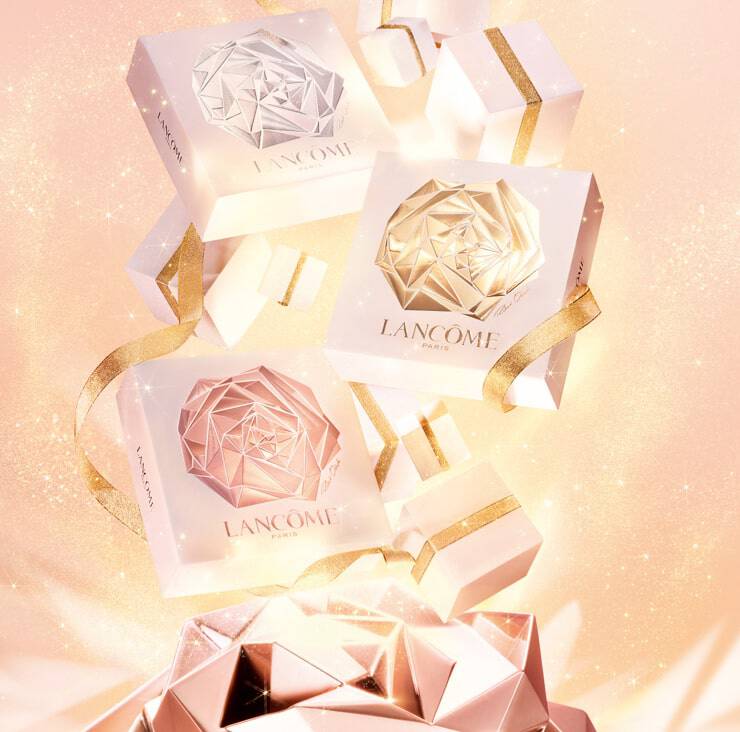 Tres cajas de regalo de Lancome con diseno geometrico en tonos blanco y dorado, adornadas con cintas brillantes sobre un fondo brillante y suave.