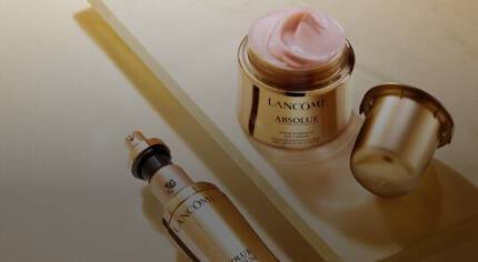 Frascos de productos de belleza de la marca Lancome, uno es un serum y el otro una crema hidratante, ambos con un acabado dorado.