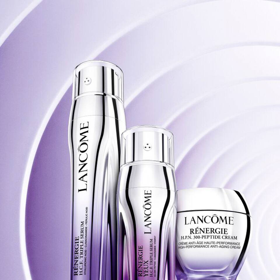 Tres productos de cuidado facial de Lancome, incluyendo suero y crema anti-edad, sobre un fondo morado suave.