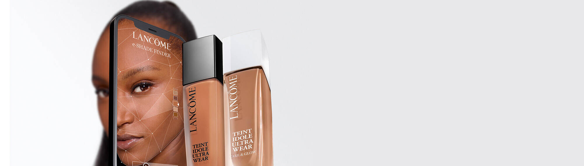 Una botella de foundation de Lancome "Teint Idole Ultra Wear" junto a un telefono que muestra un rostro femenino.