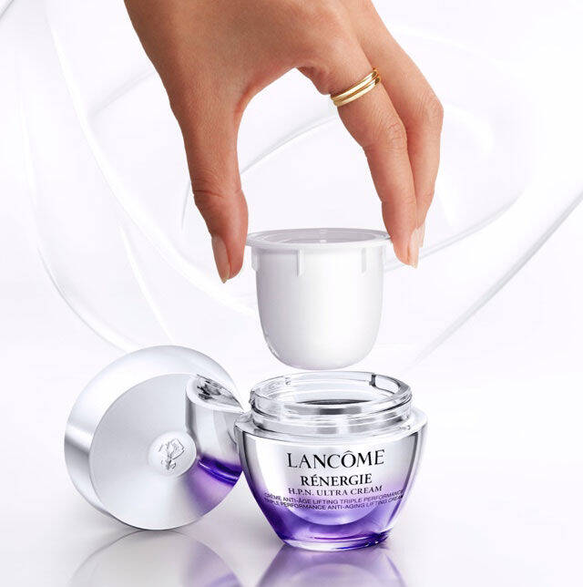 Un frasco de crema de Lancome Renergie con la tapa levantada, mientras una mano sostiene la tapa.