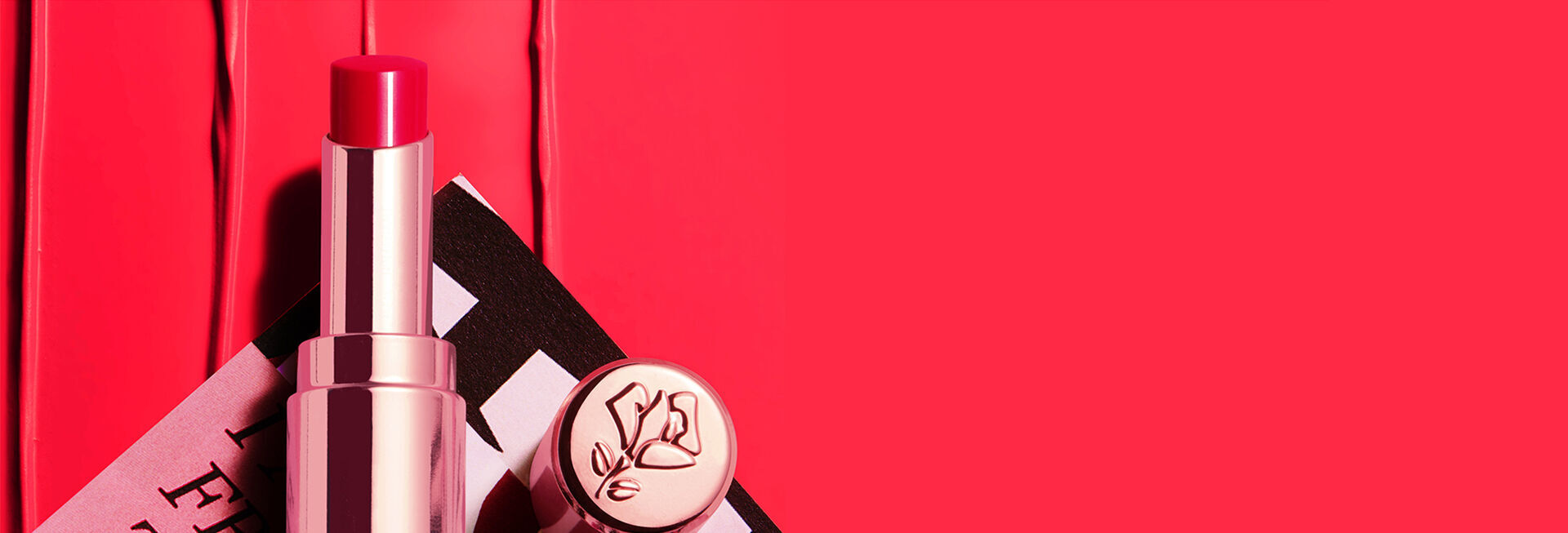 Un labial rosa brillante sobre una superficie de color rojo, acompanado de un envase elegante con el logotipo de la marca.