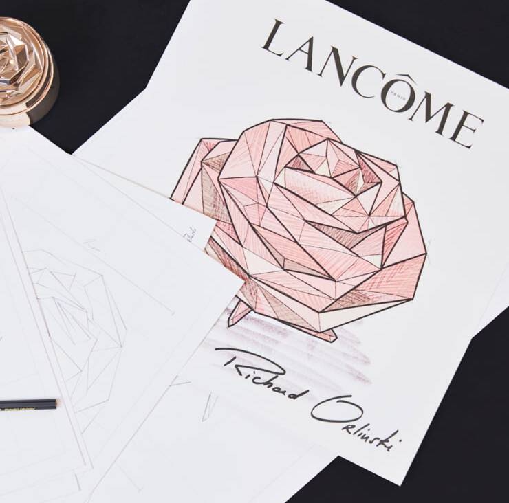Ilustracion de una rosa geometrica en tonos rosados con el logo de Lancome y la firma de Richard Orlinski, sobre un fondo de hojas de papel.