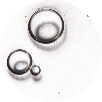 Gotas de agua sobre una superficie blanca, mostrando diferentes tamanos y reflejos en un fondo brillante.