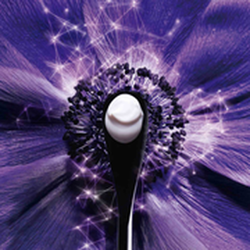Una cuchara negra que sostiene una crema blanca, en el centro de una flor morada con destellos brillantes.