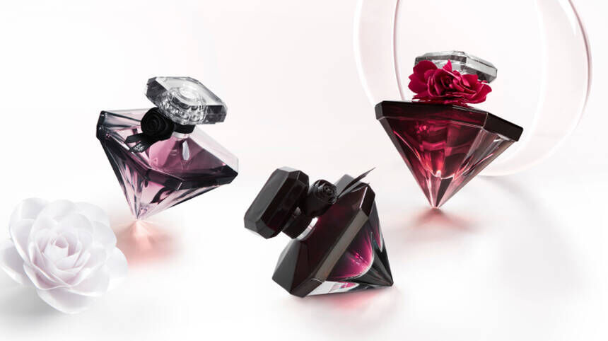 Frascos de perfumes de formas geometricas en tonos purpura y negro, con detalles de flores en la parte superior, sobre una superficie blanca.
