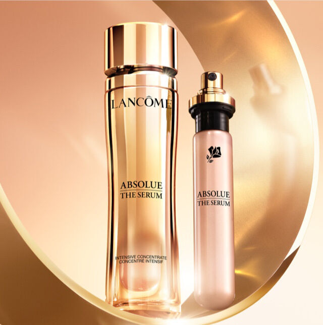 Frascos de serum de la linea "Absolue" de Lancome, uno grande y otro mas pequeno, con un fondo en tonos dorados.