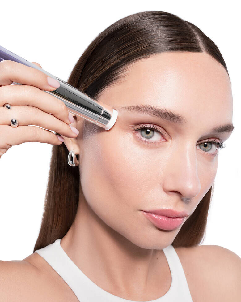 Imaginea prezintă un dispozitiv de testare a nuanței fondului de ten Lancome, plasat in fața mai multor flacoane de fond de ten Lancome, fiecare cu nuanțe diferite.