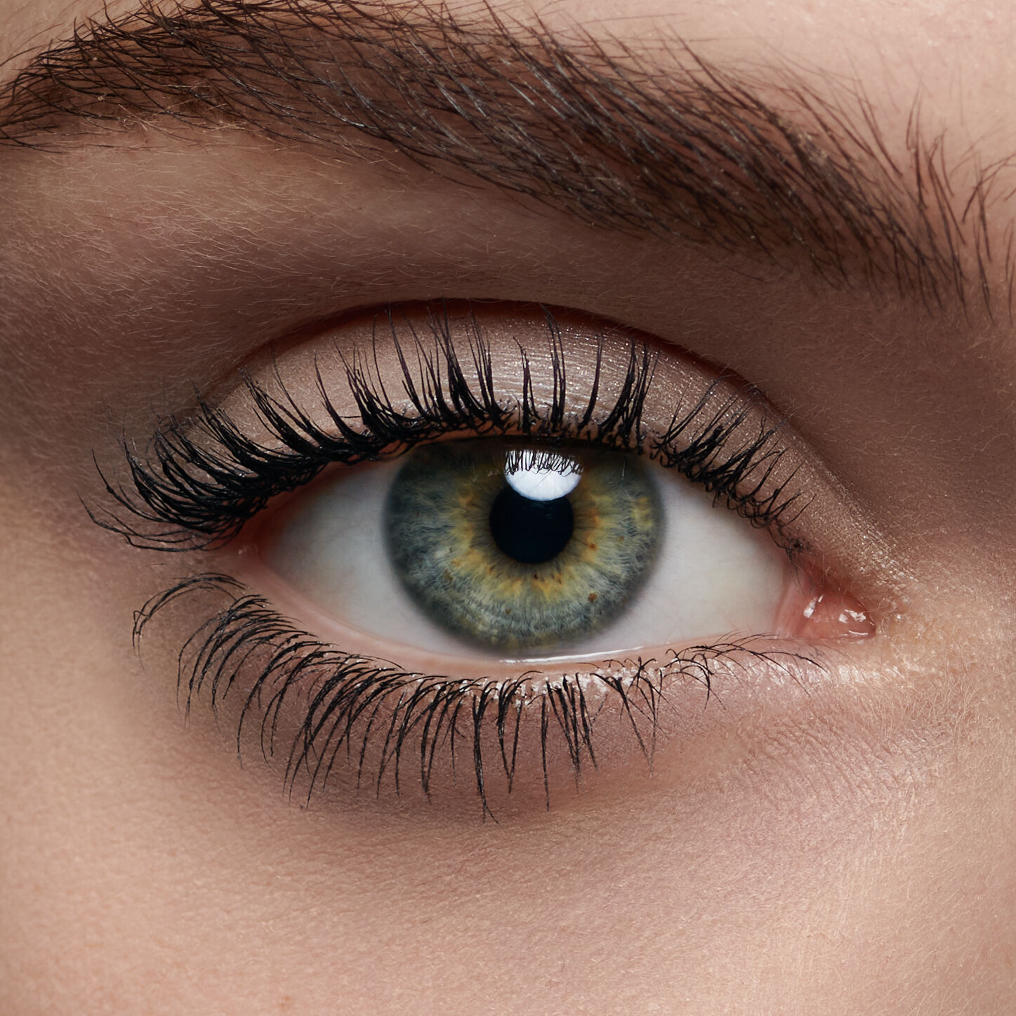 Primer plano de un ojo humano con iris de tonos verdes y amarillos, rodeado de pestanas largas y oscuras.