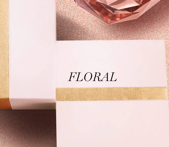 Imagen de dos cajas de regalo decoradas con cintas, una con la palabra "FLORAL" en letras grandes, y un objeto decorativo de cristal rosa en la parte superior.