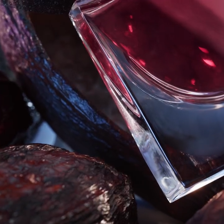 Frasco de perfume con líquido púrpura sobre un fondo de madera oscura y texturizada.